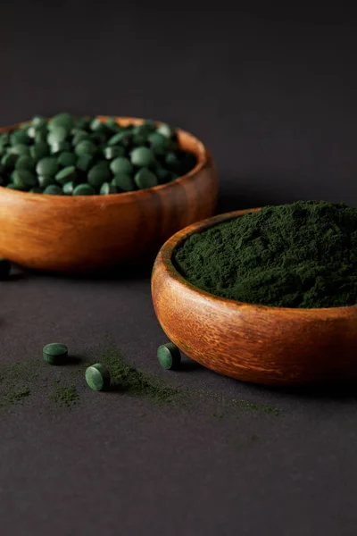 Close up view of wooden bowls with ground spirulina and spirulina in pills on grey table — Stock Photo