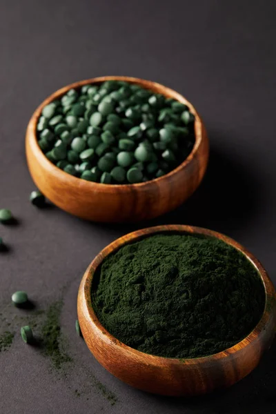 Tigelas de madeira com espirulina chão e espirulina em comprimidos sobre mesa cinza — Fotografia de Stock