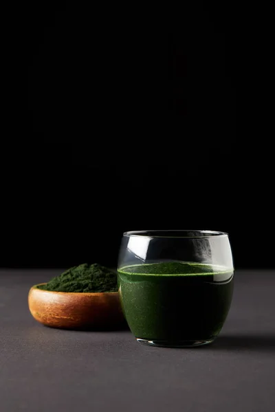 Bevanda spirulina fresca in polvere di vetro e spirulina in ciotola di legno su fondo nero — Foto stock