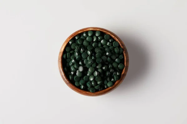 Top view of wooden bowl with pile of spirulina pills on grey table — Stock Photo