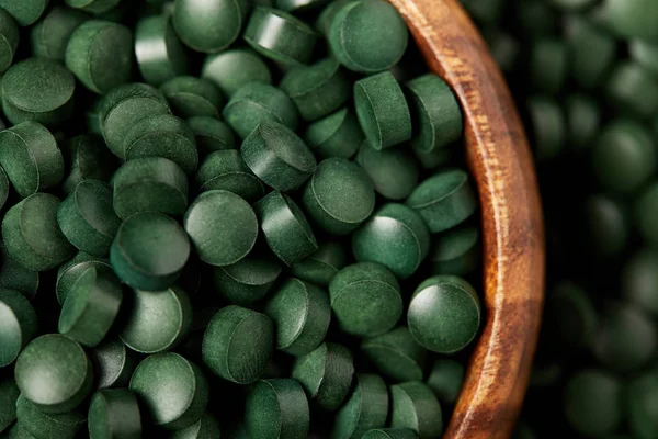 Nahaufnahme einer hölzernen Schüssel mit einem Haufen Spirulinapillen — Stockfoto