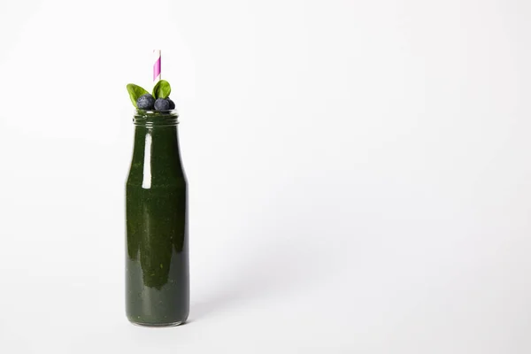 Botella de batido de espirulina con hojas de menta, arándanos y paja para beber sobre fondo blanco - foto de stock