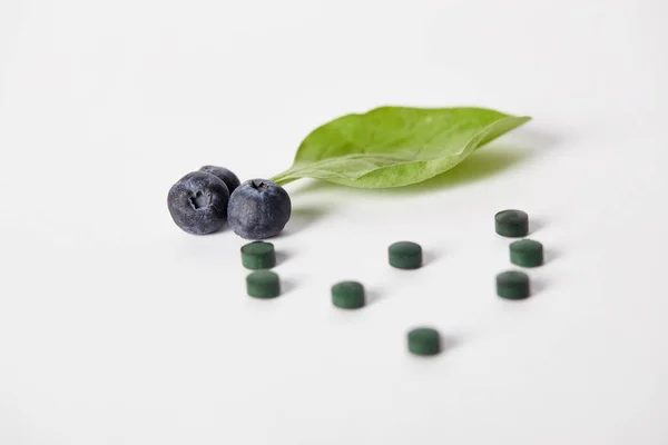 Close up view of spirulina pills, blueberries and mint leaf on white background — Stock Photo