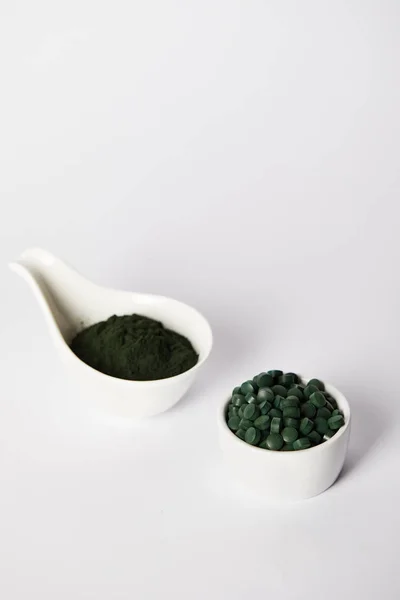 Spirulina powder and spirulina pills in bowls on grey background — Stock Photo