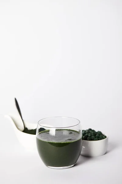 Fresh spirulina drink in glass, spoon, spirulina powder and spirulina pills in bowls on grey background — Stock Photo