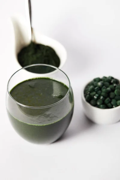 Vista da vicino della bevanda spirulina fresca in vetro, spirulina in polvere e pillole spirulina in ciotole su sfondo grigio — Foto stock