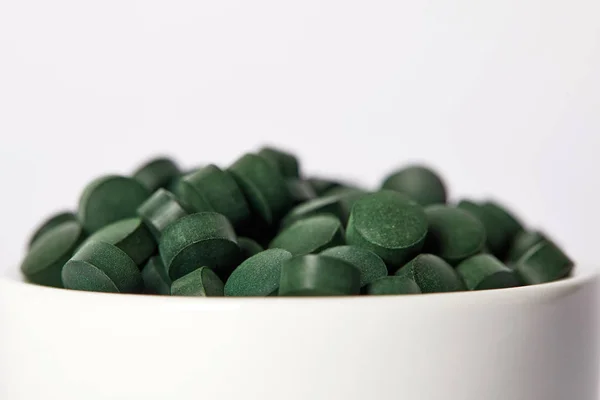 Selective focus of pile of spirulina pills in bowl isolated on grey background — Stock Photo