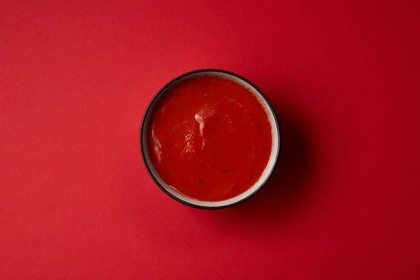 Top view of tasty red tomato soup in plate on red table — Stock Photo
