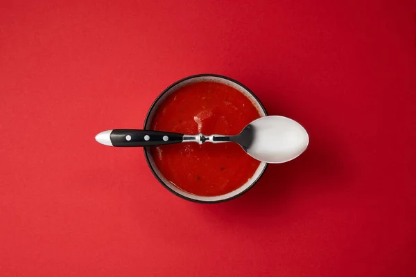 Top view of tomato soup in plate and spoon on top of plate on red table — Stock Photo