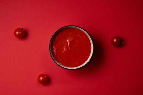 Top view of tasty tomato soup in plate and three fresh tomatoes on red table — Stock Photo