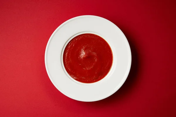 Top view of tasty tomato soup in white plate on red table — Stock Photo