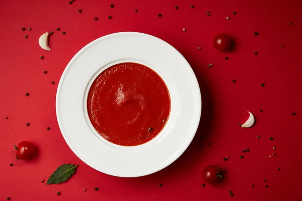 Vue du dessus de la soupe de tomates savoureuse et parsemé de poivre et de tomates sur la table rouge — Photo de stock