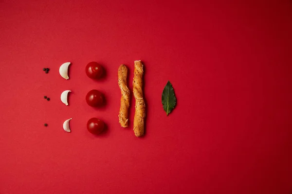 Food styling of tasty tomatoes, garlic, bread sticks and bay leaf on red table — Stock Photo