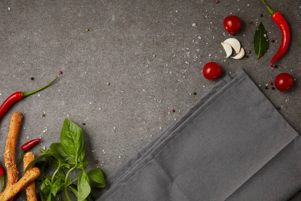 Vista superior de guardanapo cinza com legumes e paus de pão na mesa cinza — Fotografia de Stock