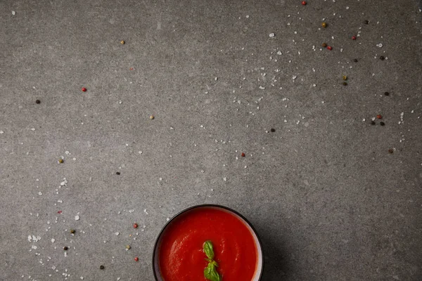 Vista dall'alto di piatto con minestra di pomodoro saporita con basilico su tavolo grigio con spezie sparse — Foto stock