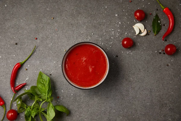 Vista dall'alto del piatto con zuppa di pomodoro, pomodori freschi, aglio e spezie sparse sul tavolo grigio — Foto stock