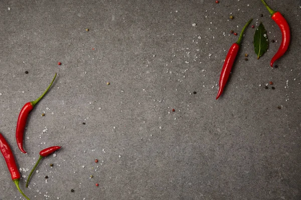 Top view of chili peppers and scattered spices on grey table — Stock Photo