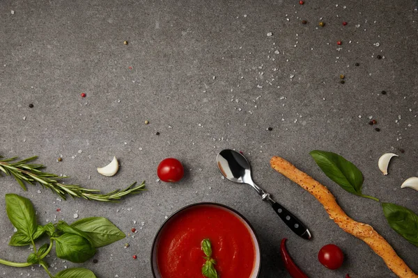 Верхний вид тарелки с вкусным томатным супом и свежими помидорами на сером столе — стоковое фото