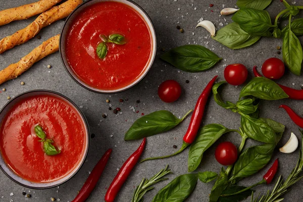 Vue du dessus des légumes, des bâtonnets de pain et de la soupe aux tomates appétissante sur la surface grise — Photo de stock