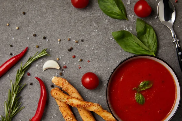 Vista dall'alto di verdure, bastoncini di pane e zuppa di pomodoro su tavola grigia — Foto stock