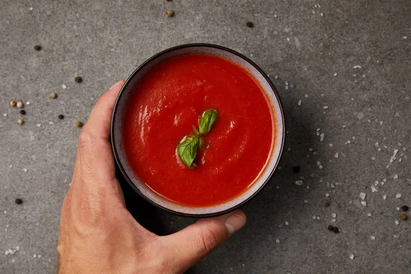 Обрезанное изображение человека, берущего тарелку с томатным супом на сером столе — стоковое фото