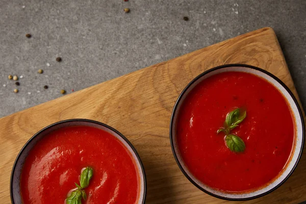 Вид зверху на дві тарілки з томатним супом на обробній дошці на сірому столі — стокове фото