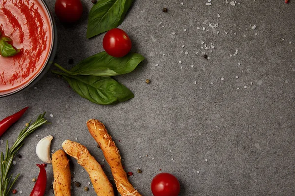 Vue du dessus de la soupe aux tomates, bâtonnets de pain et légumes sur la table grise — Photo de stock