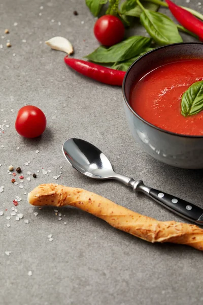 Bread stick and spoon near plate with tomato soup on grey table — Stock Photo