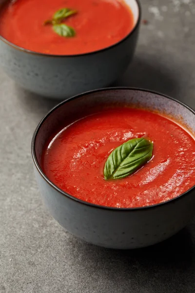 Gustosa zuppa di pomodoro rosso con basilico in piatti su tavola grigia — Foto stock