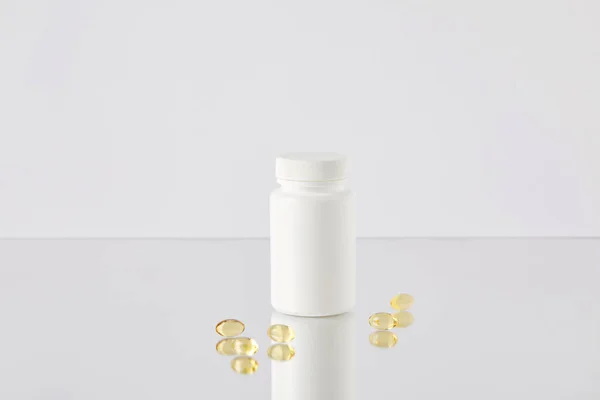 Omega fish hat supplement capsules with blank jar on reflective surface and on white — Stock Photo