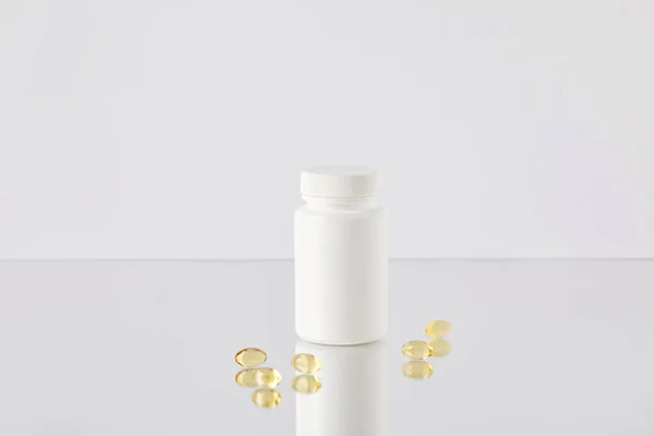 Oméga chapeau de poisson capsules de supplément avec pot vide sur la surface réfléchissante et sur blanc — Photo de stock