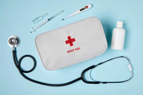 Top view of white first aid kit bag with stethoscope and medicines on blue surface — Stock Photo