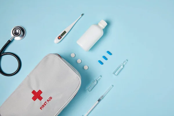 Top view of white first aid kit bag with stethoscope and various medicines on blue surface — Stock Photo