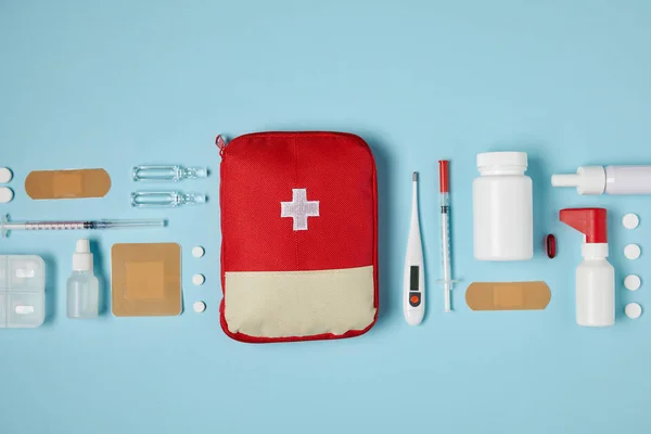 Vista superior de la bolsa roja del botiquín de primeros auxilios en la superficie azul con suministros médicos - foto de stock