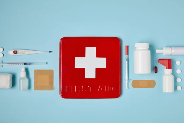 Top view of red first aid kit box on blue surface with medical supplies — Stock Photo