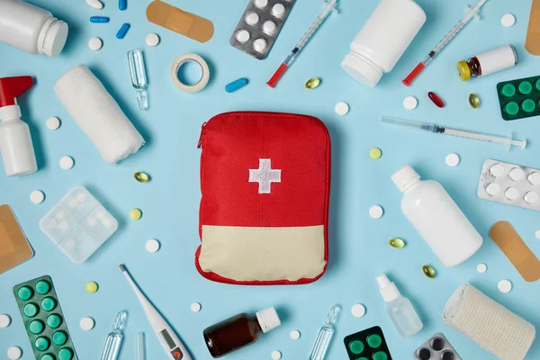 Vue du dessus du sac de trousse de premiers soins rouge sur une surface bleue entourée de différents médicaments — Photo de stock