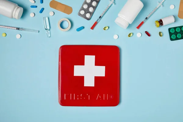 Vista dall'alto della scatola rossa del kit di pronto soccorso sulla superficie blu con vari medicinali — Foto stock