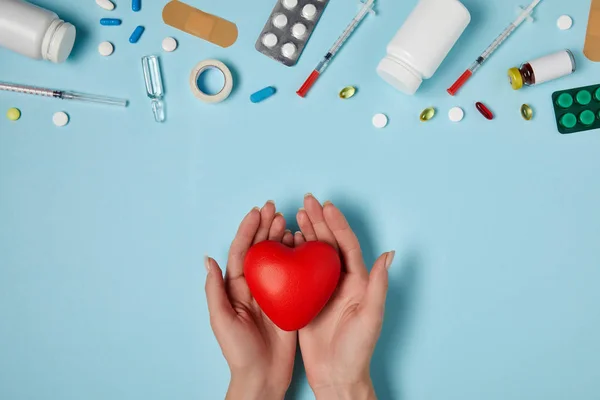 Colpo ritagliato di donna che tiene il cuore sopra i medicinali sulla superficie blu — Foto stock