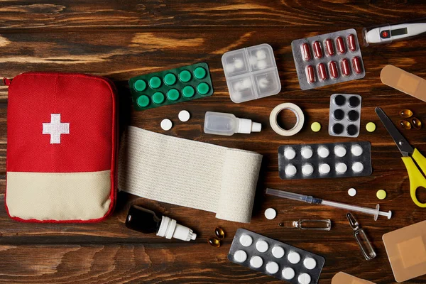 Vista superior de la bolsa del botiquín de primeros auxilios con varios medicamentos en la mesa de madera - foto de stock