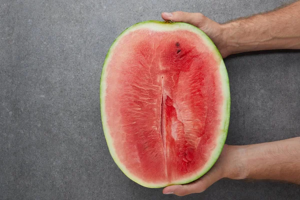 Partial view of man holding watermelon cut half in hands on grey concrete tabletop — Stock Photo