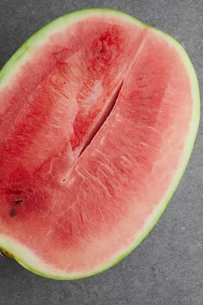 Draufsicht auf frische Wassermelone, die zur Hälfte auf grauer Betonplatte geschnitten ist — Stockfoto