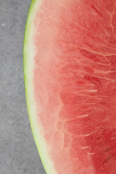 Draufsicht auf frische Wassermelone, die zur Hälfte auf grauer Betonplatte geschnitten ist — Stockfoto