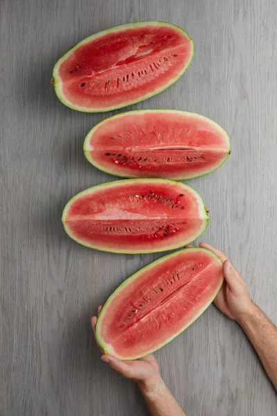 Partial view of male hands and fresh watermelon slices on grey wooden tabletop — Stock Photo