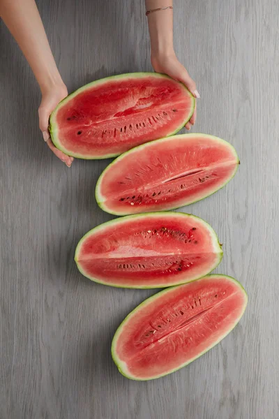 Abgeschnittene Aufnahme weiblicher Hände und frische Wassermelonenscheiben auf grauer Holzoberfläche — Stockfoto