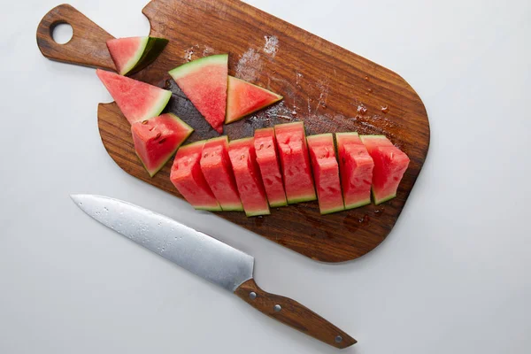 Food composition with fresh watermelon slices arranged on wooden cutting board and knife on white surface — Stock Photo