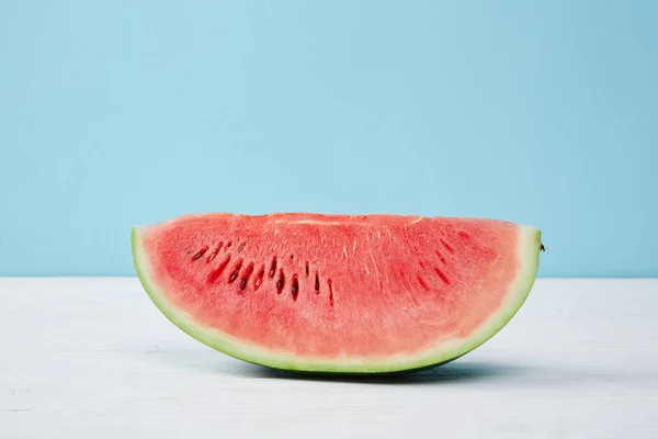 Nahaufnahme der frischen Wassermelonenscheibe auf weißer Oberfläche auf blauem Hintergrund — Stockfoto