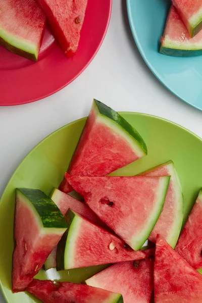 Flach mit Wassermelonenscheiben auf bunten Tellern auf weißer Tischplatte — Stockfoto