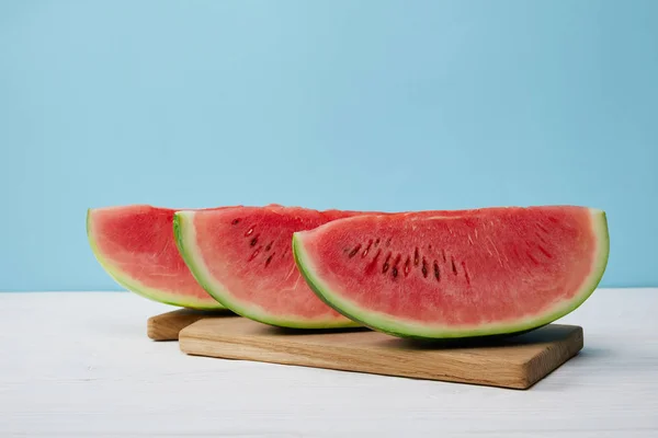 Nahaufnahme arrangierter Wassermelonenscheiben auf Schneidebrett auf weißer Oberfläche vor blauem Hintergrund — Stockfoto