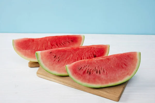 Nahaufnahme arrangierter Wassermelonenscheiben auf Schneidebrett auf weißer Oberfläche vor blauem Hintergrund — Stockfoto