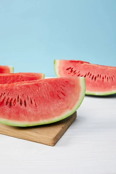 Close up view of arranged watermelon slices on cutting board on white surface on blue backdrop — Stock Photo